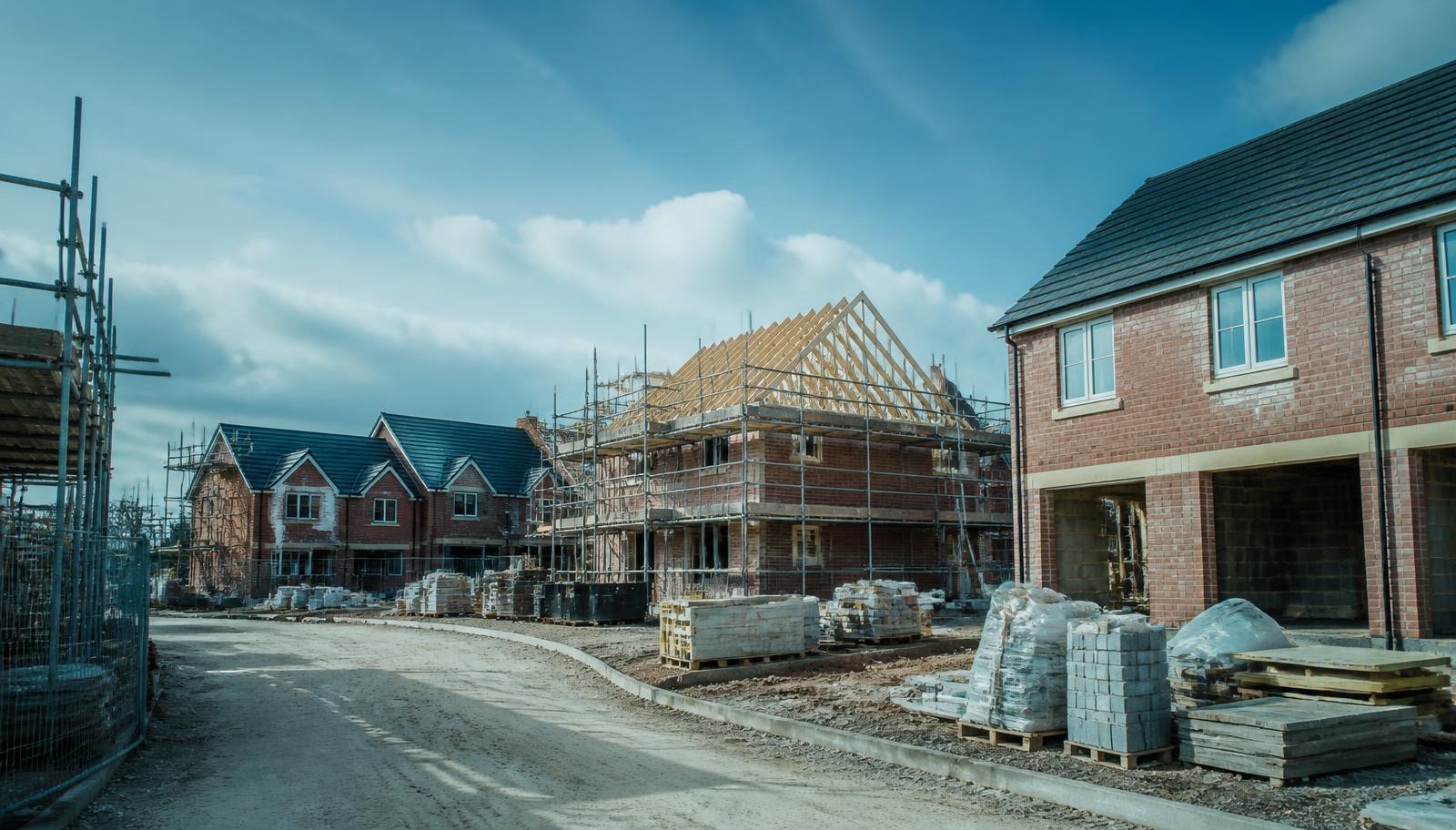 UK housing development under construction, with brick houses at several stages and scaffolding along a site road