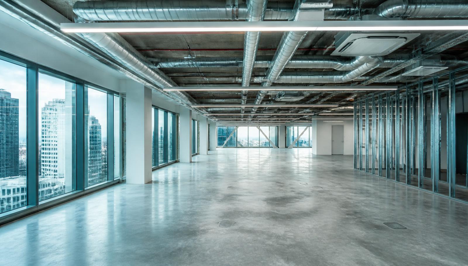 Empty modern office floor being fitted out, with exposed ductwork, linear LED lighting and a glazed facade