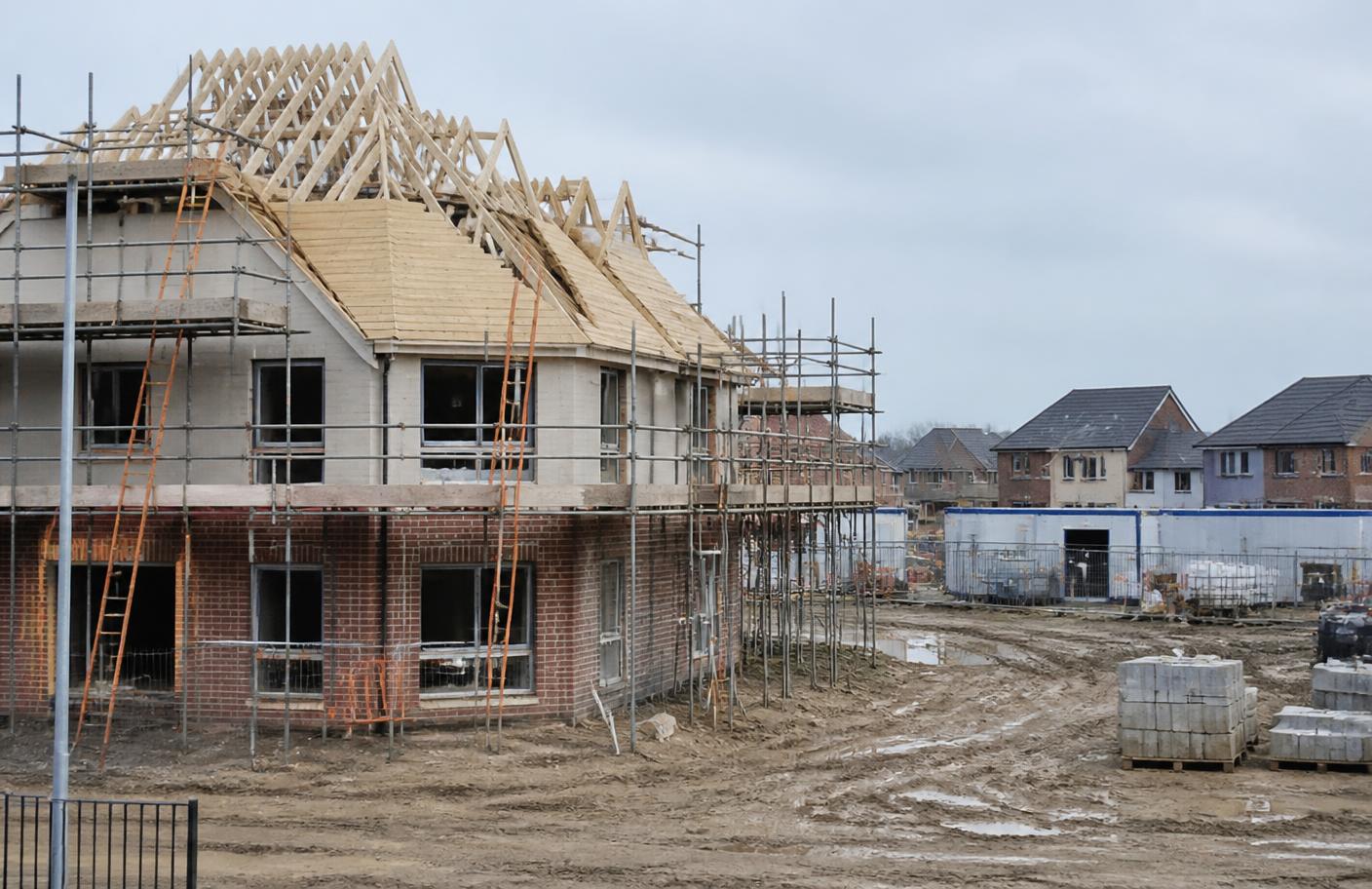 New houses under construction with scaffolding and exposed roof trusses on a UK development site