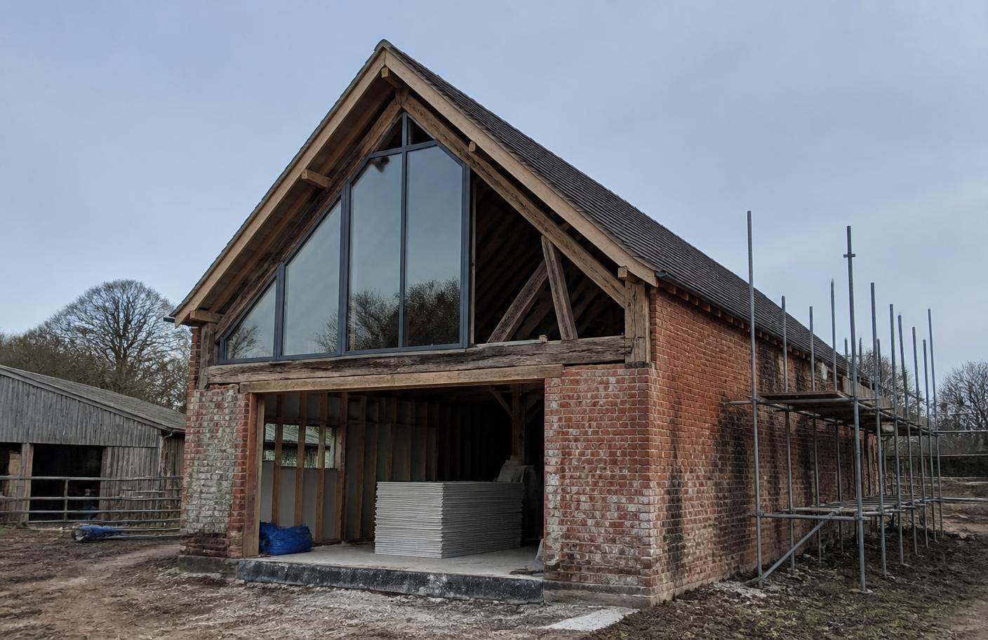 Brick and timber barn part-way through conversion into a home, with a new glazed gable